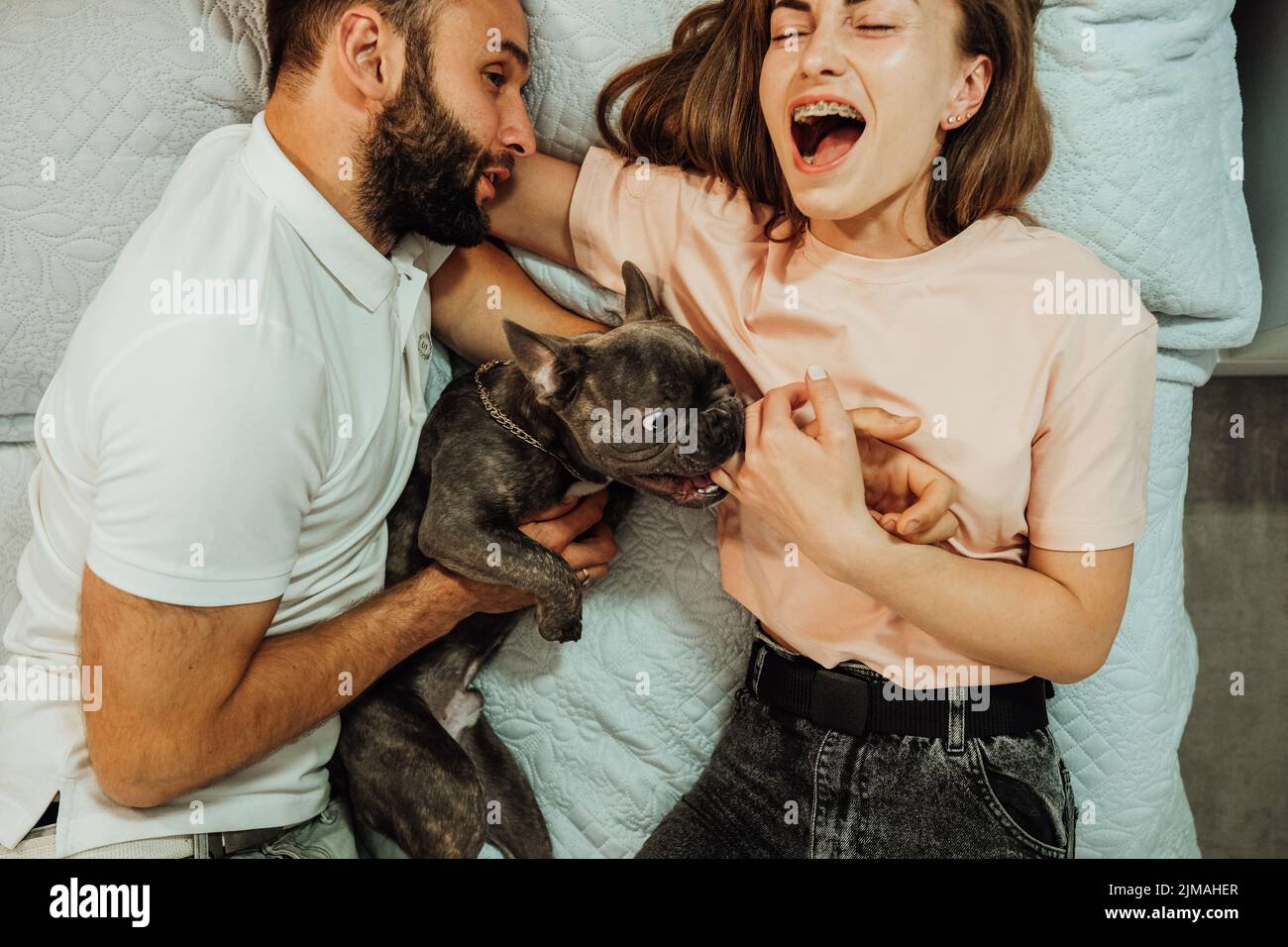 Bulldog français mordent le doigt de la femme pendant qu'ils sont sur le lit avec l'homme Banque D'Images
