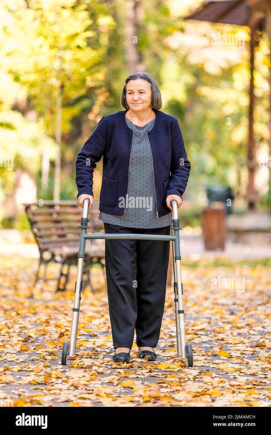 Femme avec walker walking outdoors in autumn park Banque D'Images