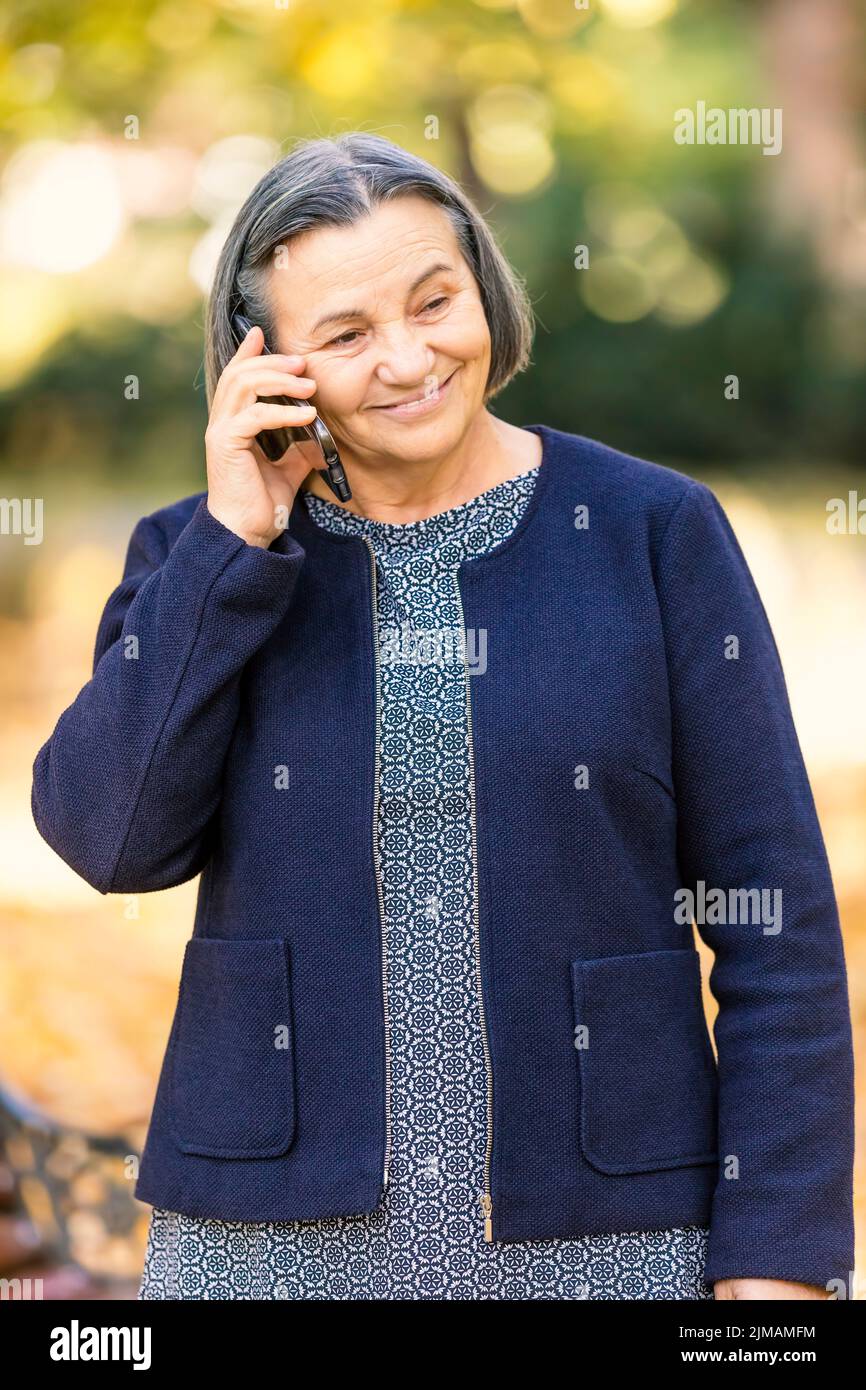 Senior Positive Woman talking on smartphone outdoors Banque D'Images