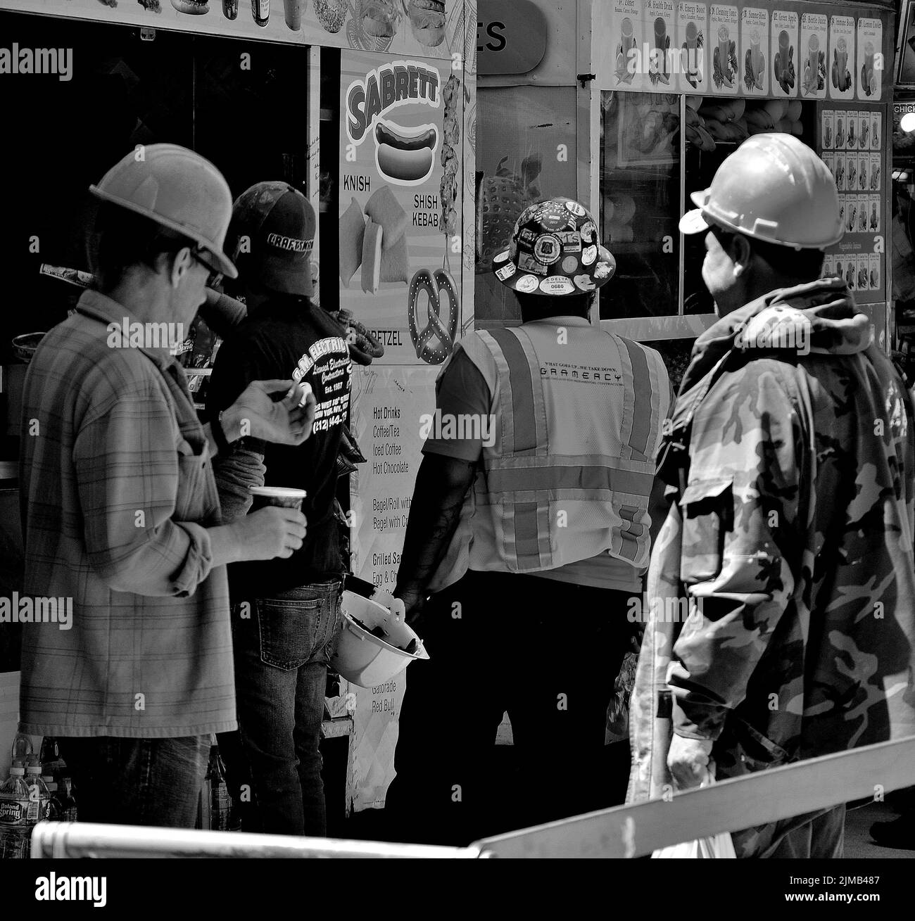 Une photo en échelle de gris des ouvriers du bâtiment qui s'arrêtent pour un déjeuner dans un stand de hot dog à New York, aux États-Unis Banque D'Images