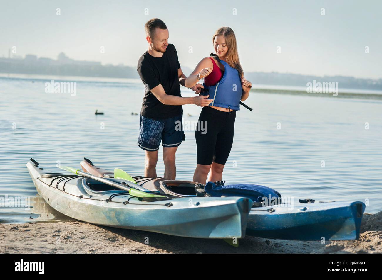 l'homme met la femme en gilet de sauvetage pour aller kayak, vacances d'été, sport actif, sécurité Banque D'Images