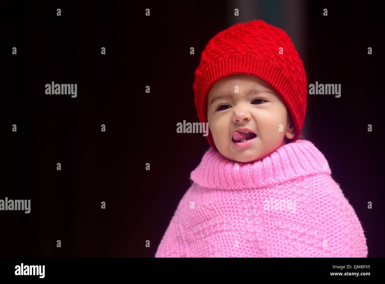 Une adorable petite fille indienne de 13 mois portant une casquette d'hiver rouge et un poncho Banque D'Images