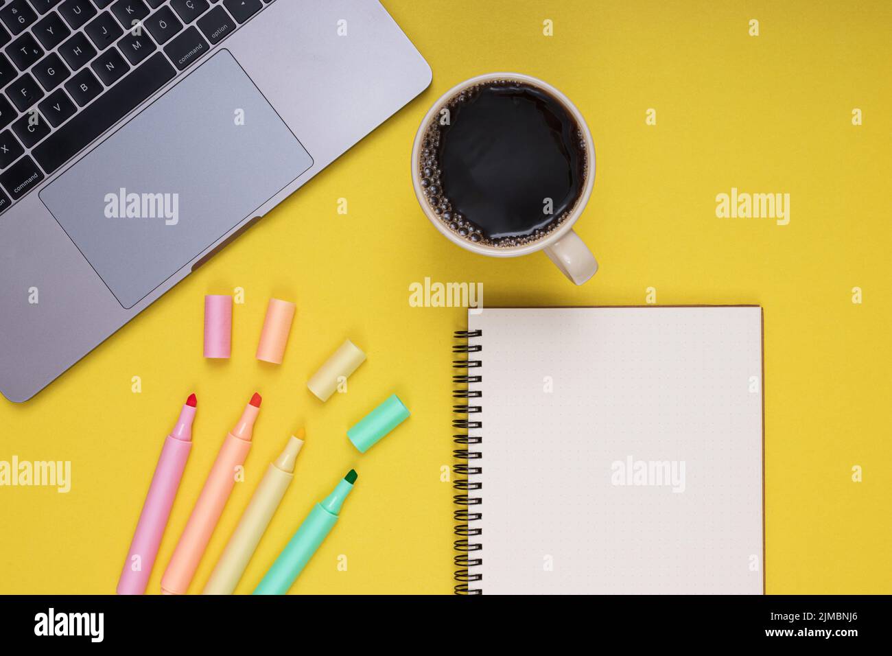 Ordinateur portable, bloc-notes, crayons de couleur, tasse à café. Retour à l'école. Arrière-plan jaune isolé Banque D'Images