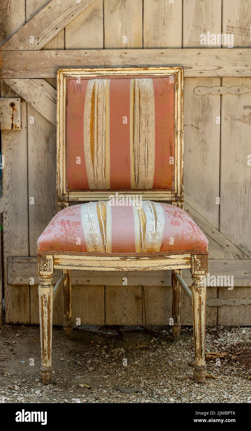 chaise ancienne chic et rembourrée avec peinture décolorée et laissée à l'extérieur contre une porte en bois rustique. ancienne chaise laissée en pourriture, style chic et sordide. Banque D'Images
