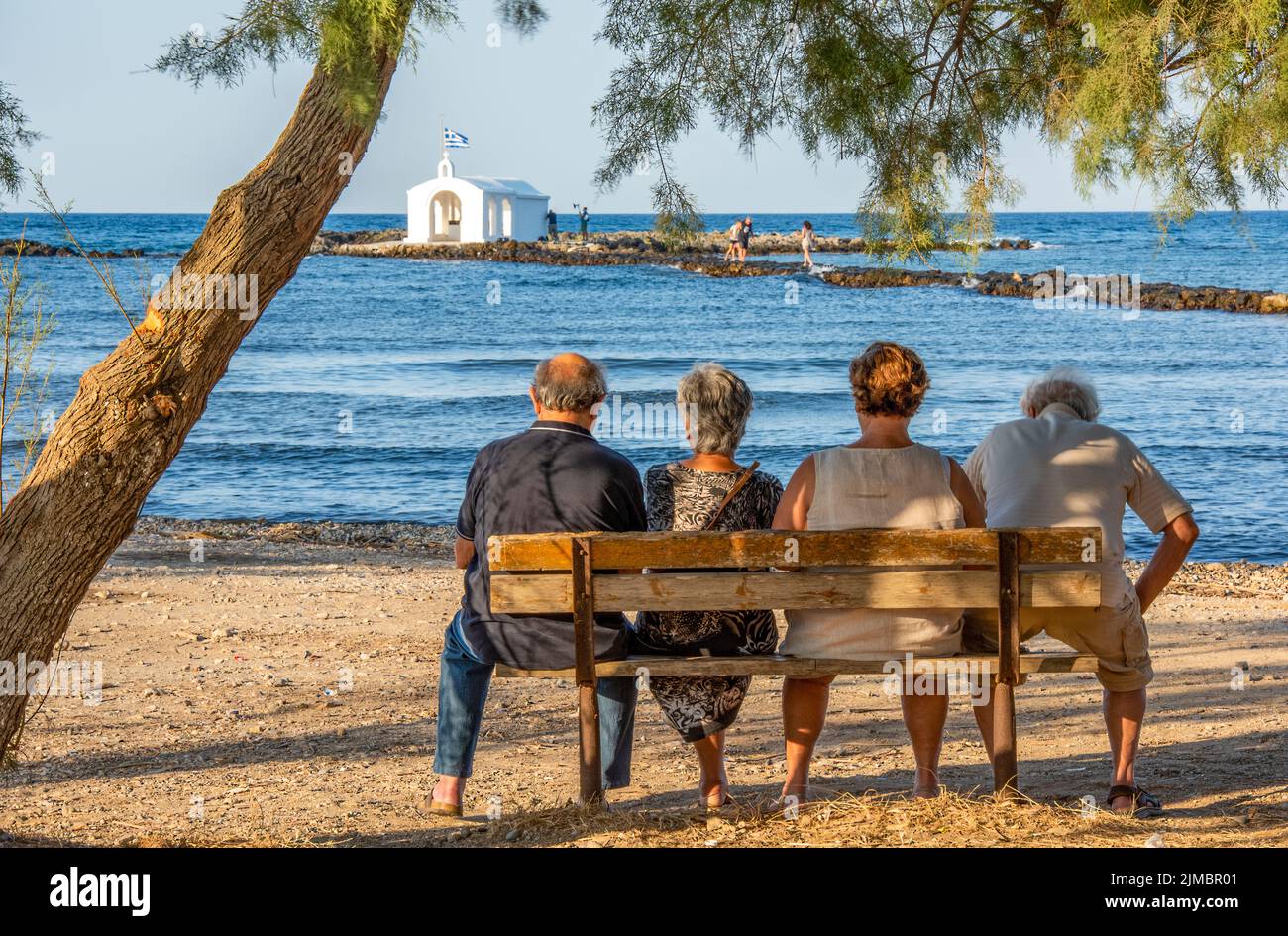 quatre retraités plus âgés assis dans le sahde d'un arbre donnant sur la mer sur l'île grecque de crète, deux couples assis sur un banc en bois Banque D'Images