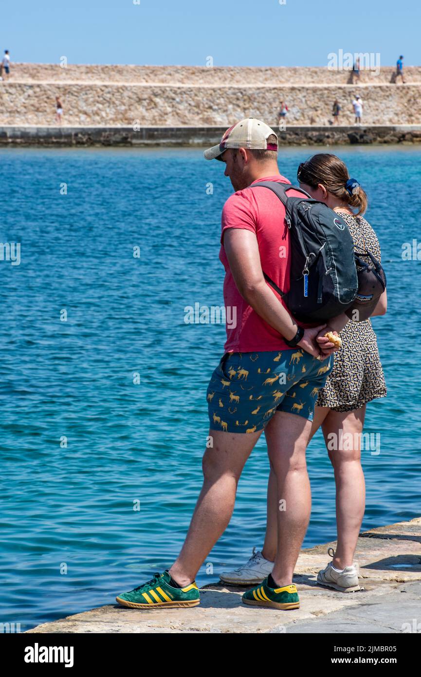 un jeune couple en vacances en grèce sur l'île grecque de crète se tenant sur le côté de l'eau à côté du port de chania, en regardant de l'autre côté de l'eau. Banque D'Images