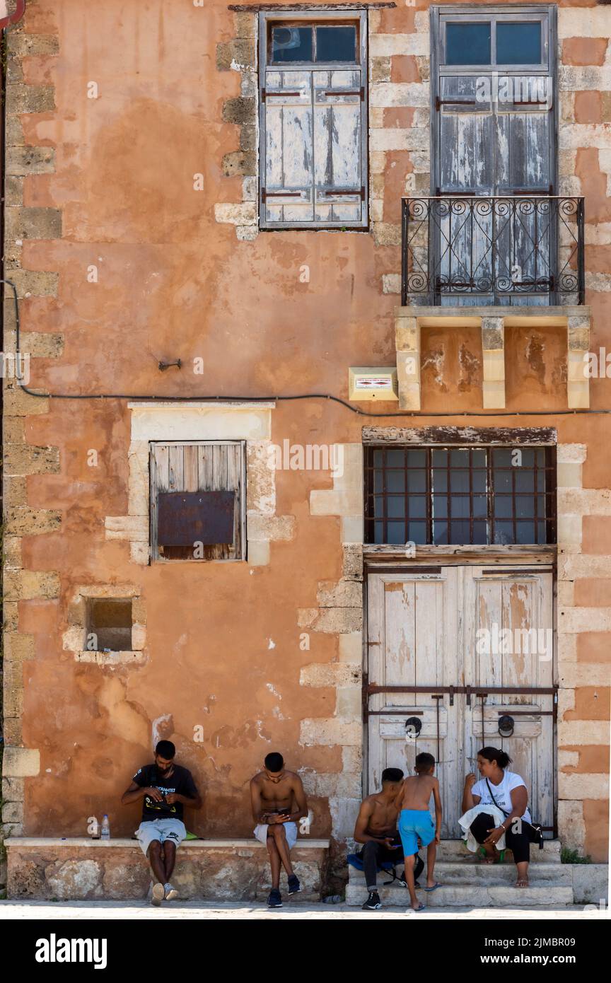les familles locales se ombrageant du soleil de midi à côté d'un vieux bâtiment grec traditionnel sur l'île de crète dans la ville de chania. Banque D'Images