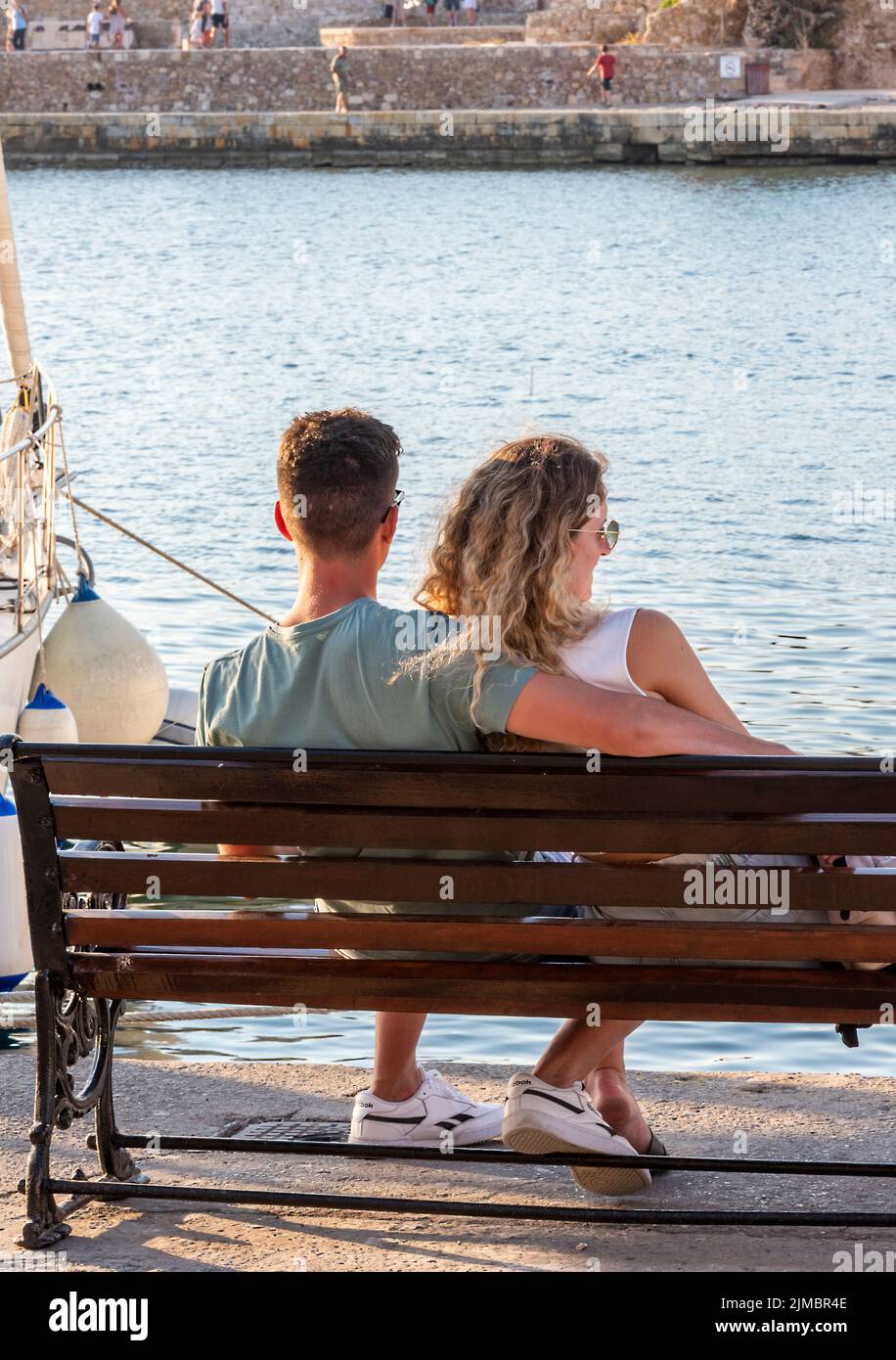 un jeune couple d'amoureux assis sur un banc au bord de la mer donnant sur le port de chania, sur l'îlot grec de crète Banque D'Images