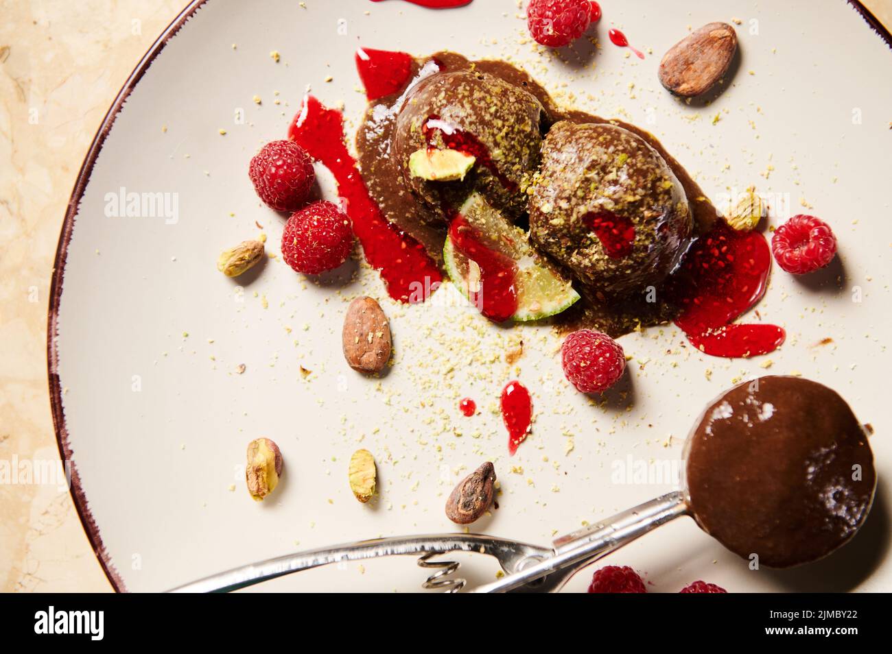 Vue de dessus d'une pelle en métal pour sorbet, avec glace au chocolat maison, sans lait, garnie de pistaches râpées, framboises, fèves de cacao et d'être Banque D'Images