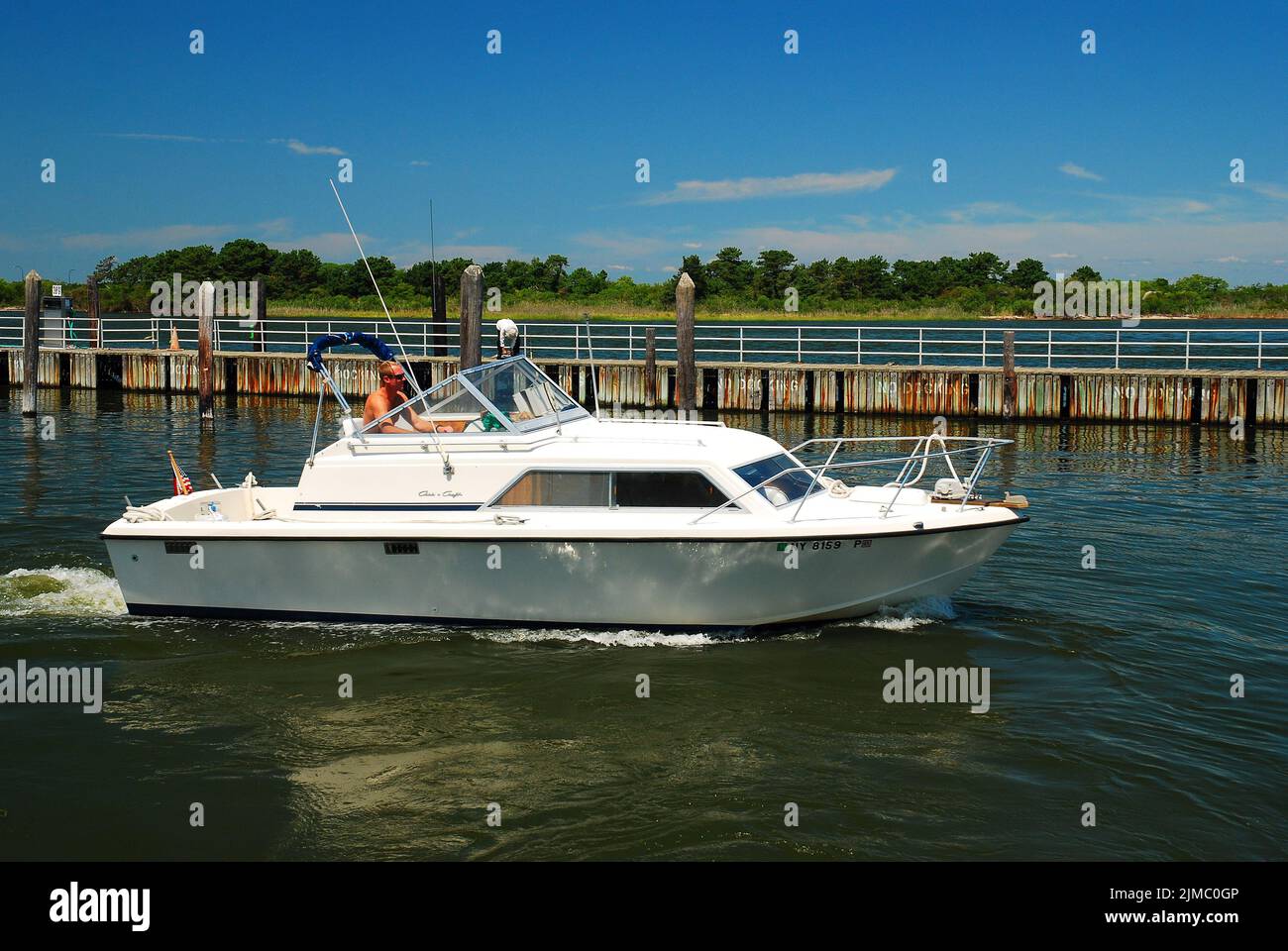 Un homme adulte vole son bateau hors d'une marina lors d'une belle journée de vacances d'été ensoleillée Banque D'Images