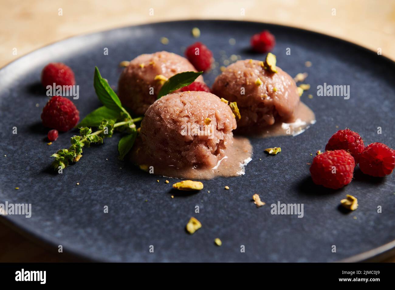 La nourriture reste vie. Boules de sorbet aux baies, garnies de pistaches, framboises et feuilles de citron basilic sur une assiette bleue Banque D'Images