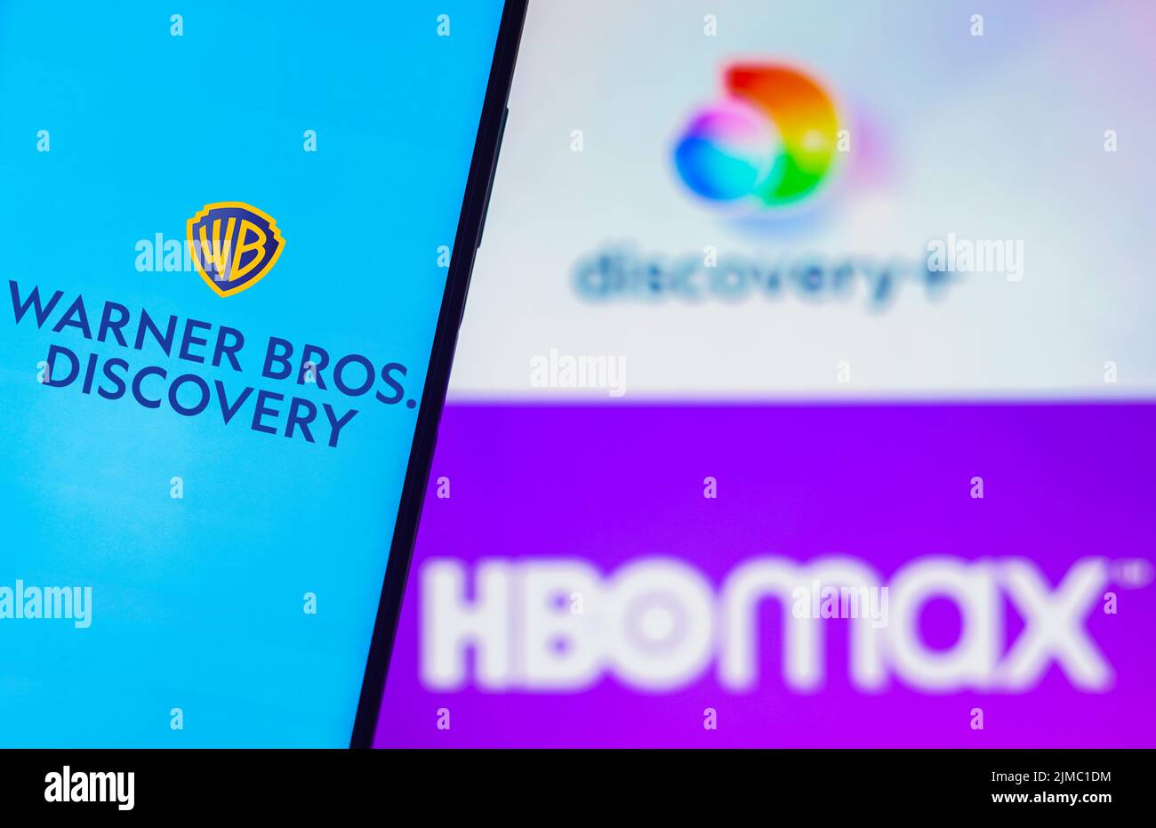 Dans cette illustration, le logo Warner Bros. Discovery s'affiche sur l'écran d'un smartphone et en arrière-plan, les logos HBO Max et Discovery plus Banque D'Images