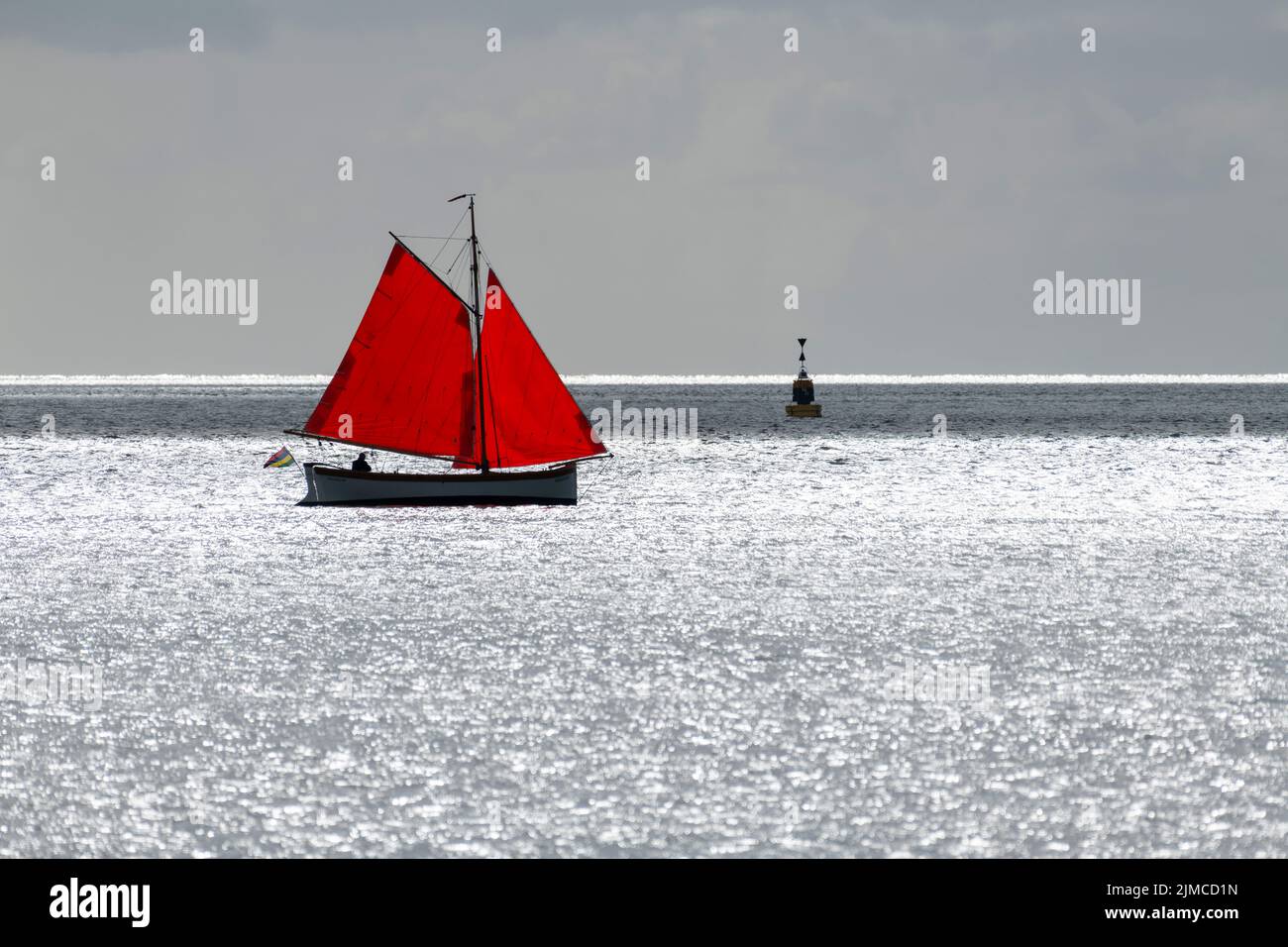 Bateau à voile avec voile rouge contre l'éblouissement du soleil Banque D'Images
