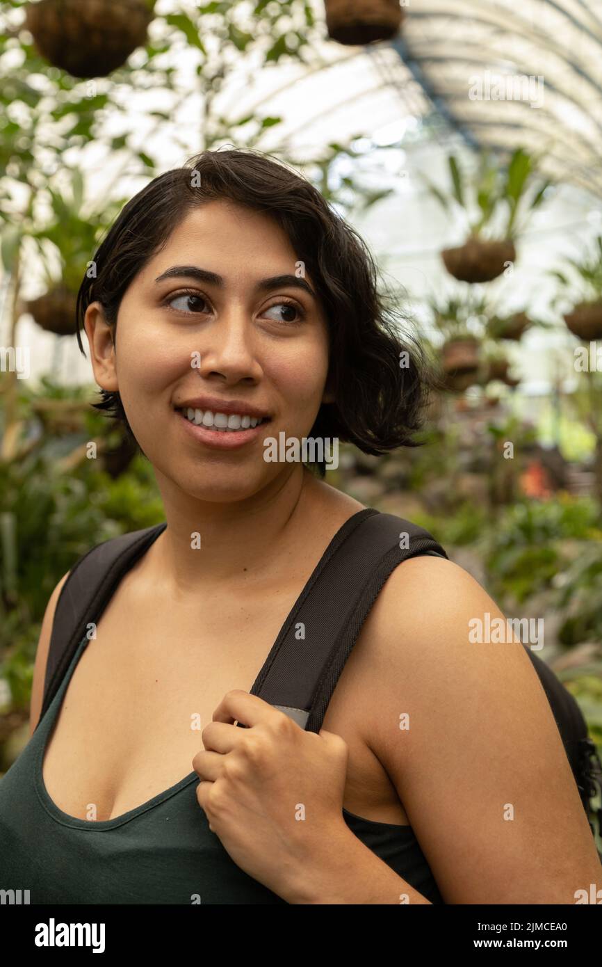 jeune femme latine gaie aux cheveux courts, style de vie de voyageur avec des plantes en arrière-plan, jardin et beauté naturelle Banque D'Images