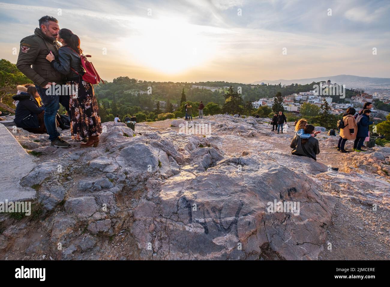 Quelques touristes s'embrasser contre le cadre romantique d'un coucher de soleil sur une colline à travers le rocher de l'Acropole à Athènes. Banque D'Images