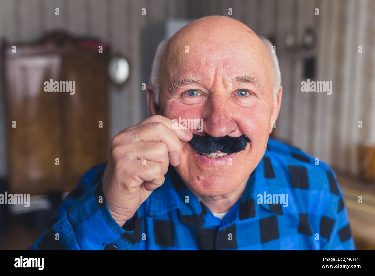 Joyeux drôle caucasien senior homme tenant la fausse moustache noire et souriant à la caméra, s'amuser en retraite . Photo de haute qualité Banque D'Images