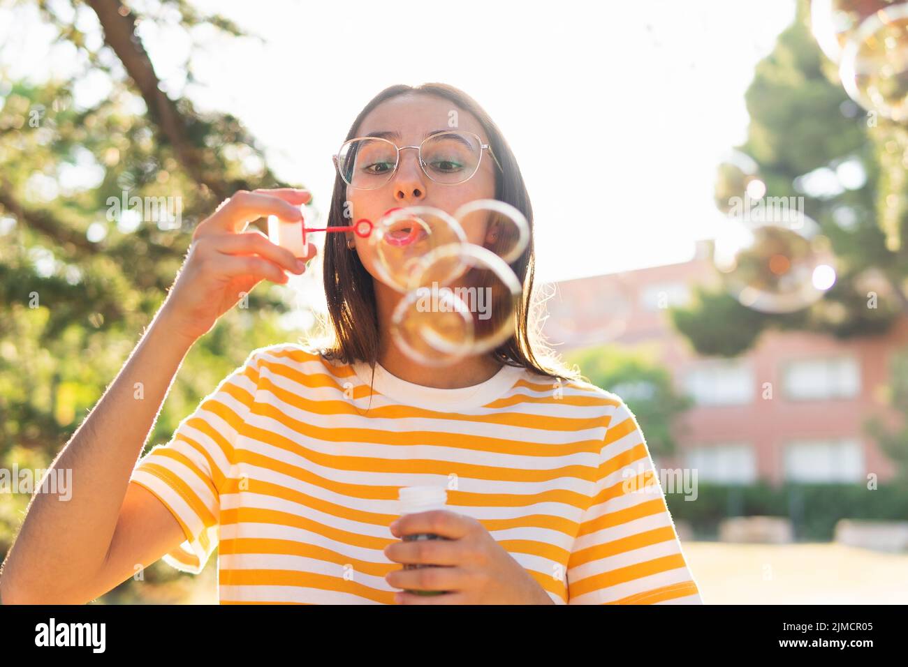 Jeune brune en t-shirt rayé et des verres soufflant des bulles de savon tout en passant le week-end ensoleillé dans le parc vert en été Banque D'Images