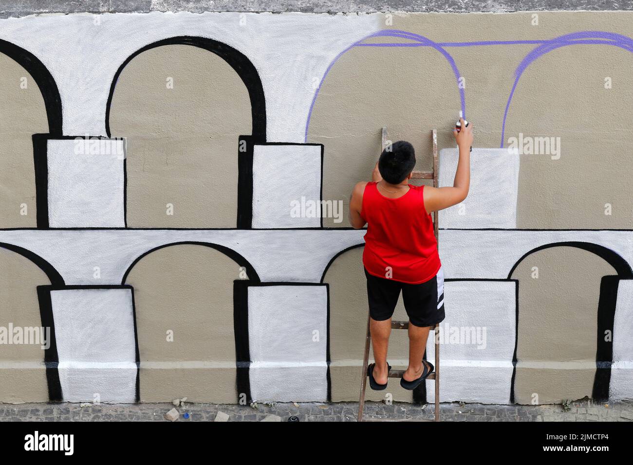 Homme peint graffiti mural d'Arcos da Lapa. Artiste de rue créant un travail de design moderne Banque D'Images