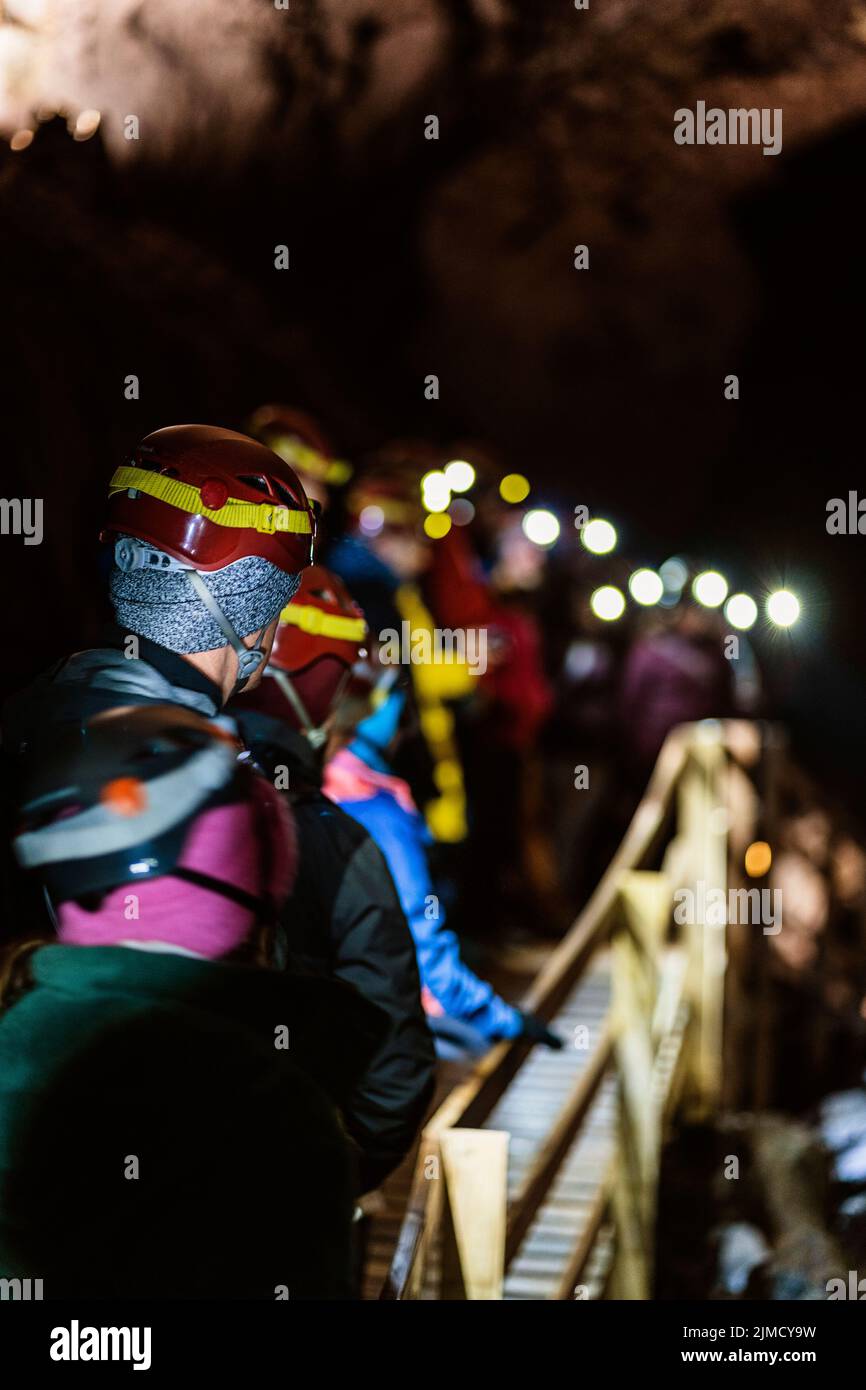 Groupe de voyageurs méconnaissables vêtues de vêtements chauds et de casques de protection marchant sur une passerelle en bois lors d'une randonnée dans la grotte d'Islande Banque D'Images