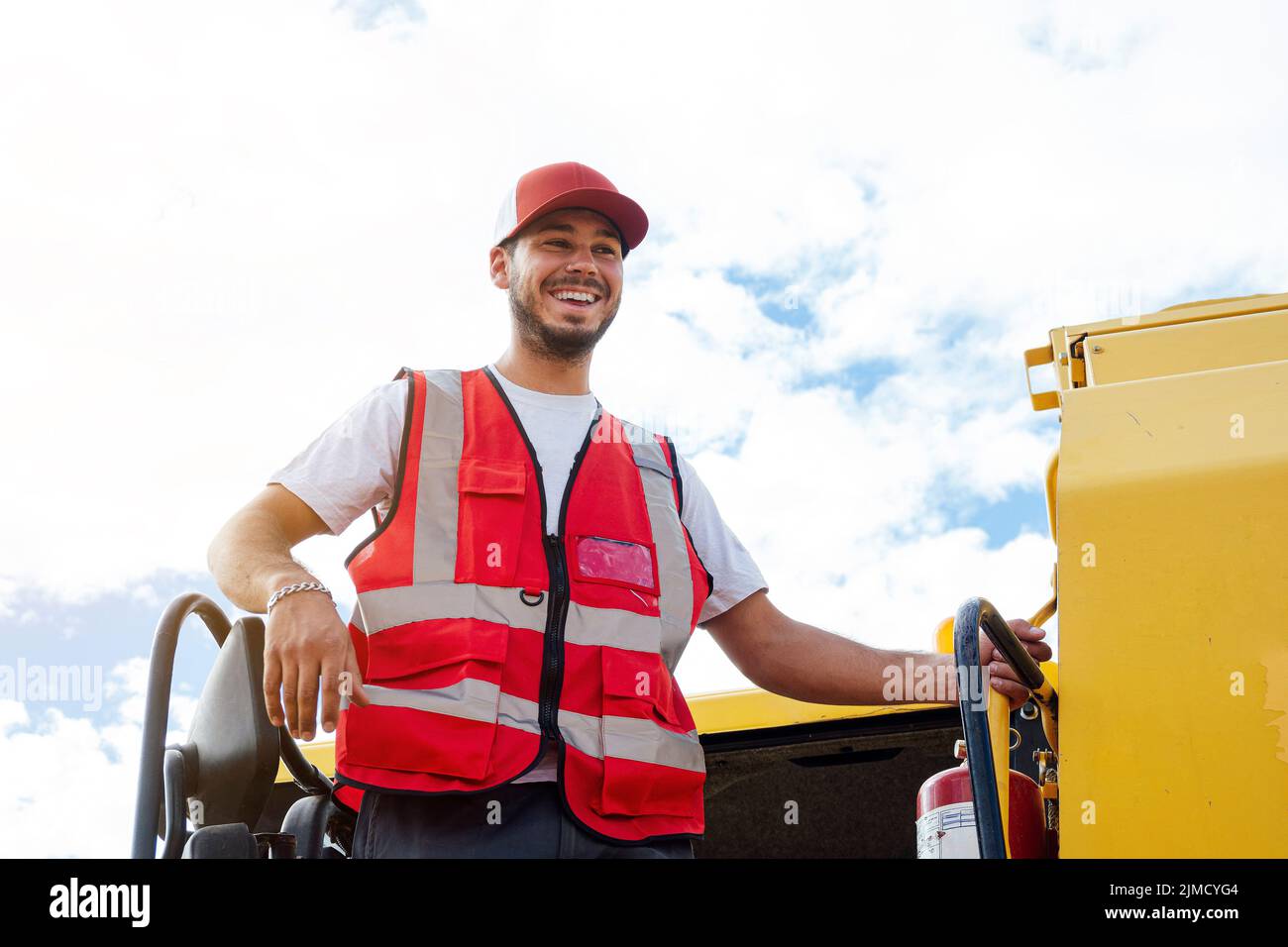 Depuis le bas, un homme joyeux se tient debout et regarde loin sur l'échelle de la machine professionnelle pour recueillir les grains dans les fie agricoles Banque D'Images