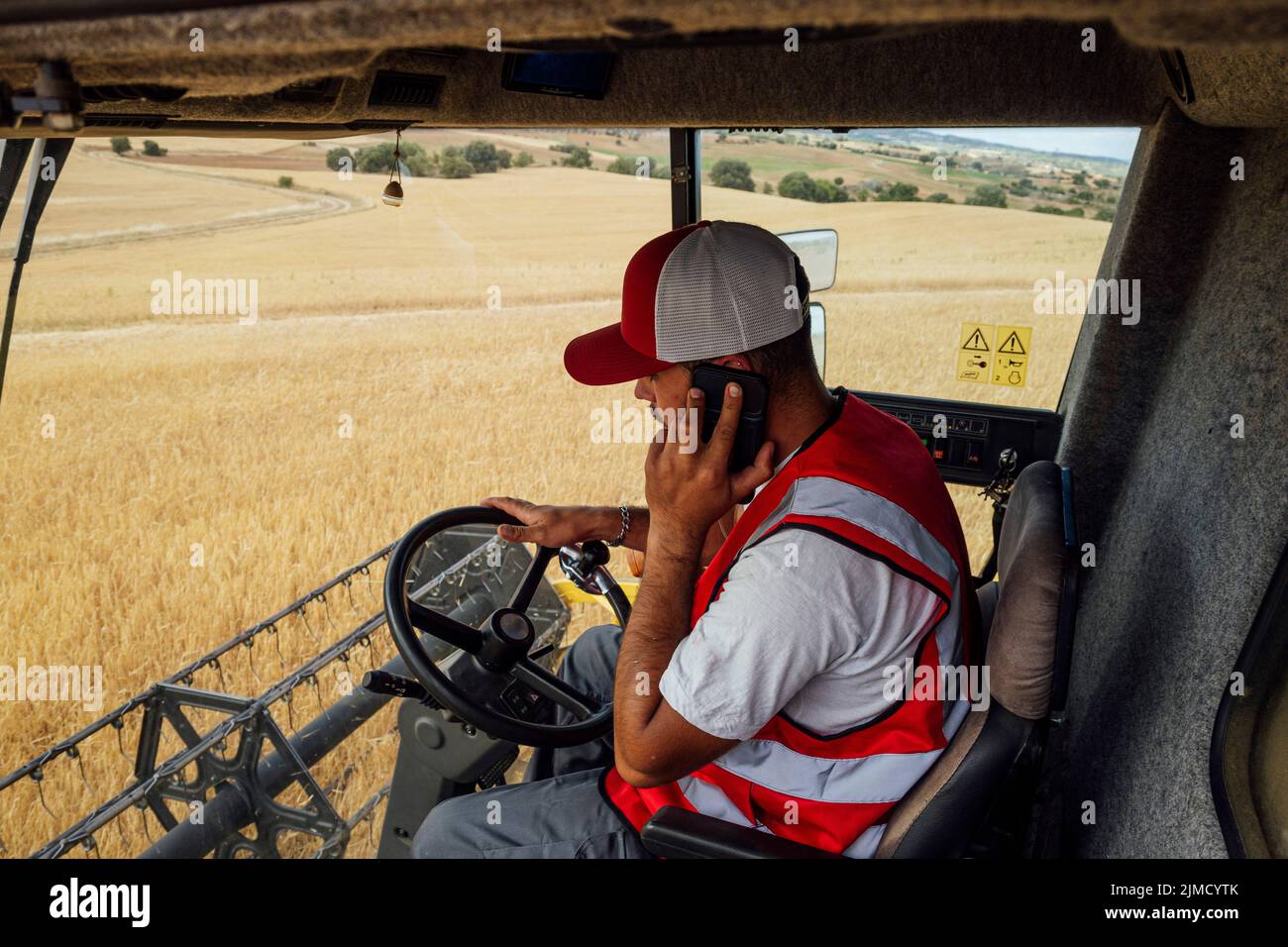 Vue latérale de l'opérateur de moissonneuse-batteuse mâle parlant sur smartphone lors de la récolte de grains de blé dans une machine industrielle professionnelle dans un champ agricole Banque D'Images