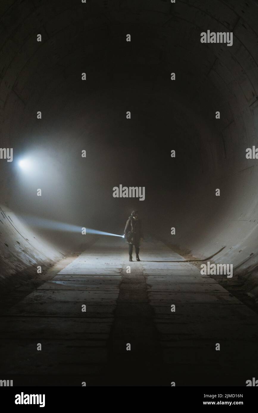 Personne avec une lampe de poche illuminant l'obscurité et explorant un tunnel souterrain grundy avec des murs en béton pendant l'apocalypse Banque D'Images