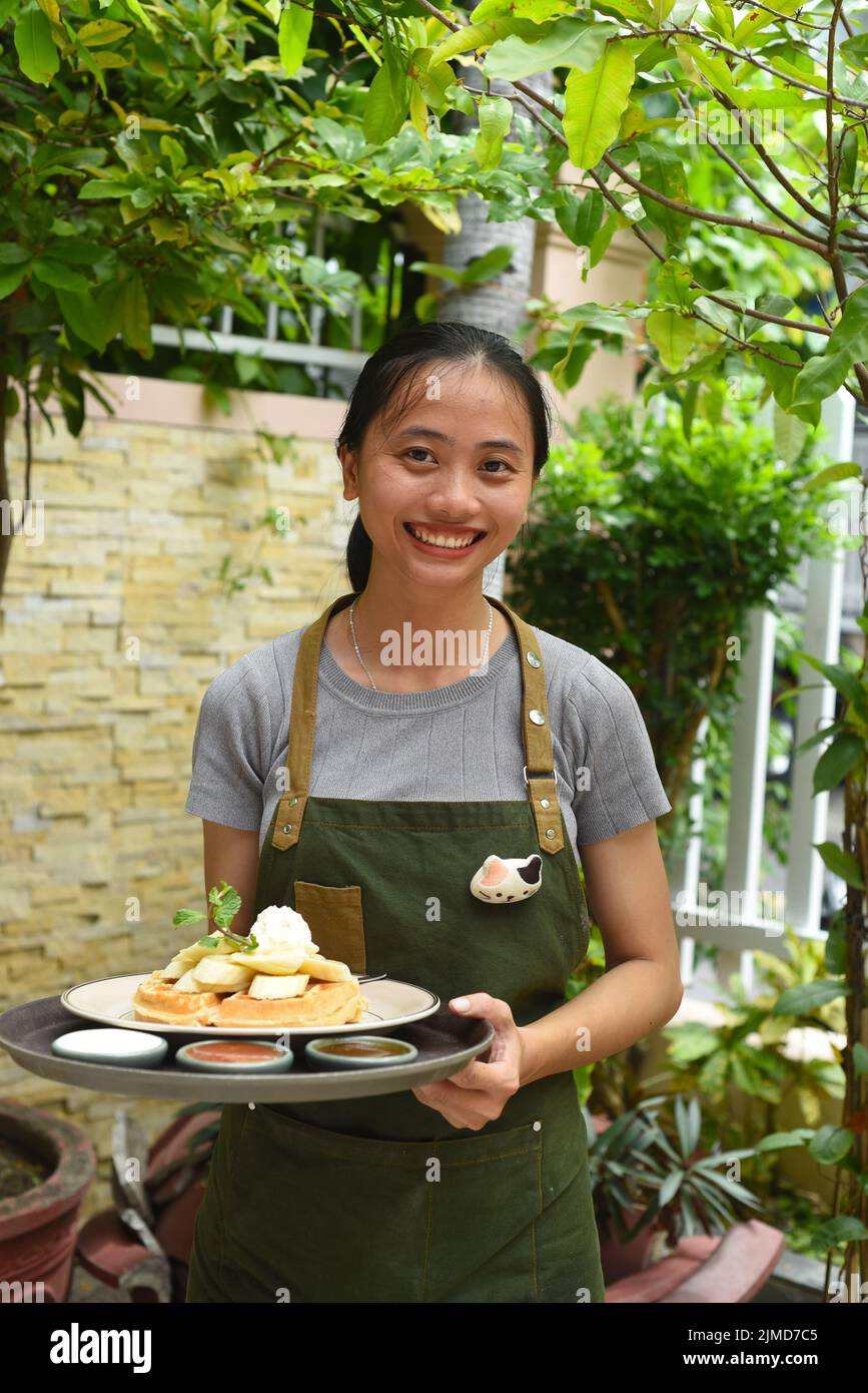 Une serveuse vietnamienne sert des gaufres belges avec des fruits et de la crème glacée dans un café extérieur Banque D'Images