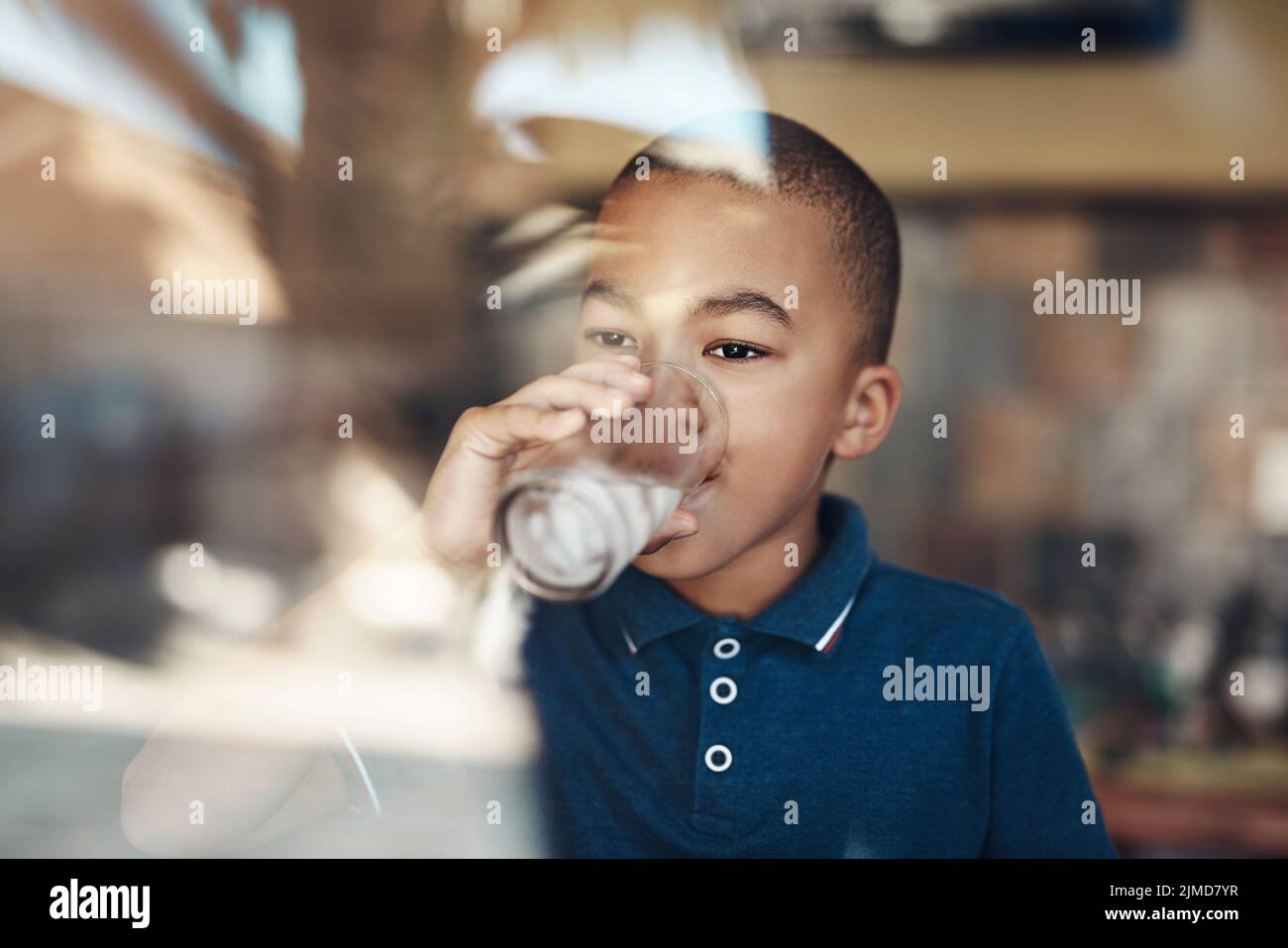 L'eau me maintient en bonne santé. Un jeune garçon boit un verre d'eau à la maison. Banque D'Images