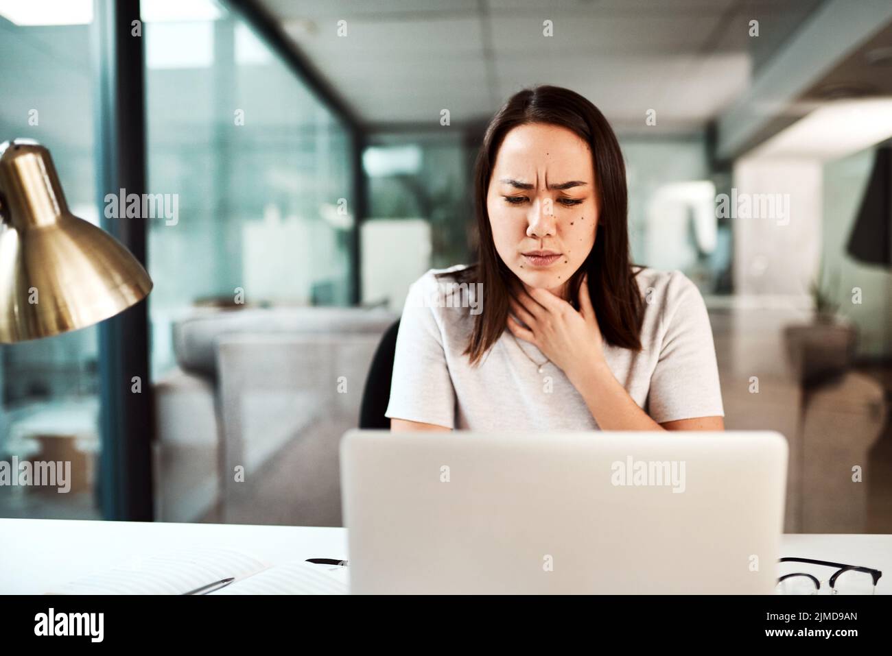 J'ai besoin de quelque chose pour apaiser ce mal de gorge. Une jeune femme d'affaires qui souffre d'un mal de gorge pendant qu'elle travaille dans un bureau. Banque D'Images