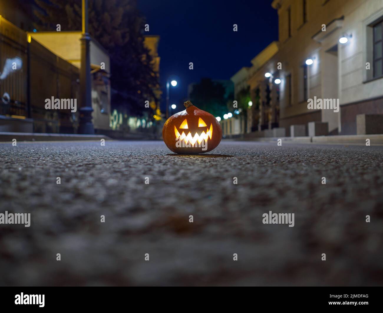 Halloween citrouille sur l'asphalte dans une rue déserte de la ville la nuit. Lumières de ville et vieux bâtiments de couleur floue. Banque D'Images