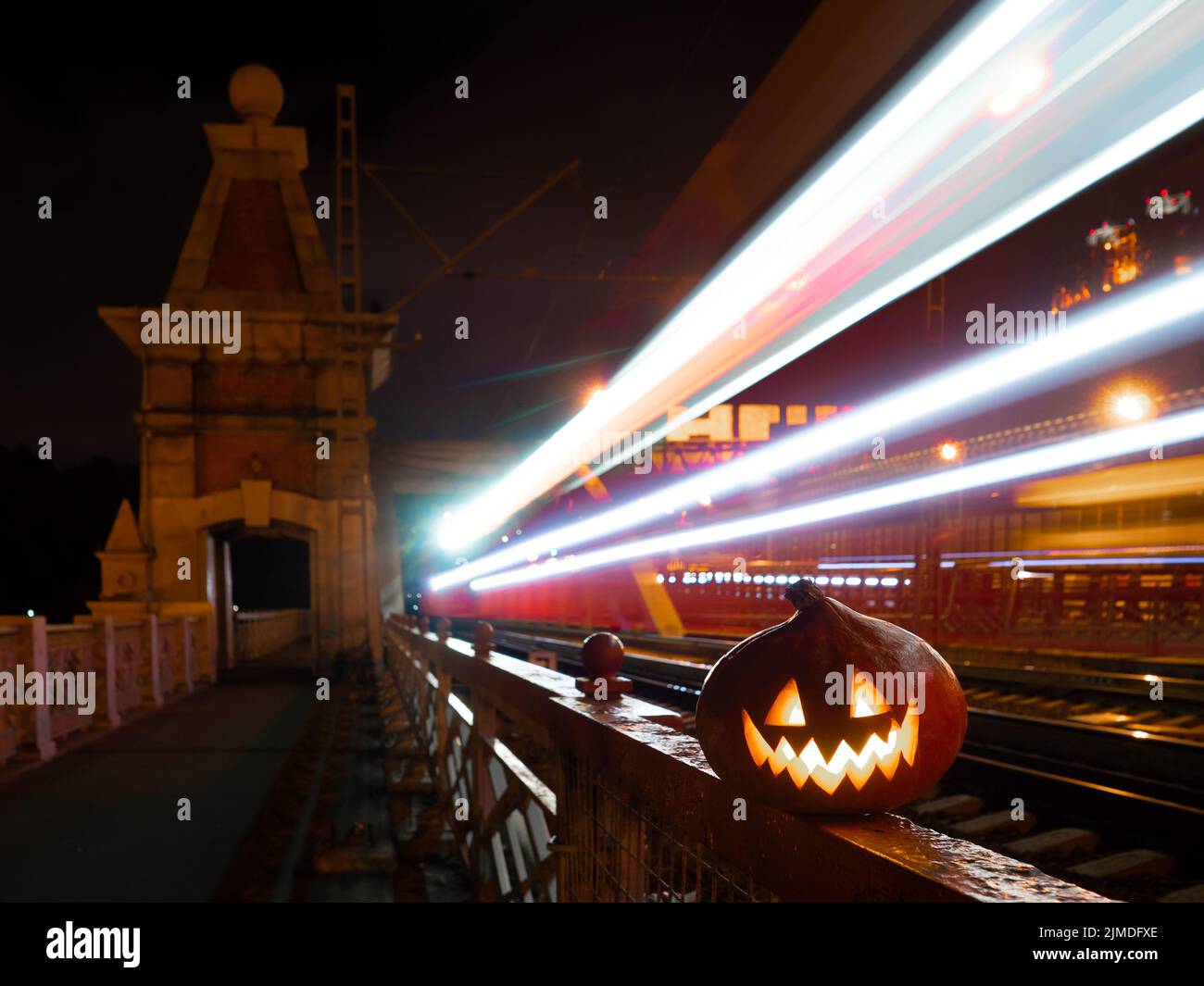 Citrouille d'Halloween avec une grimace lumineuse la nuit sur le pont de chemin de fer. En arrière-plan, il y a des rails et des traînées floues de Banque D'Images