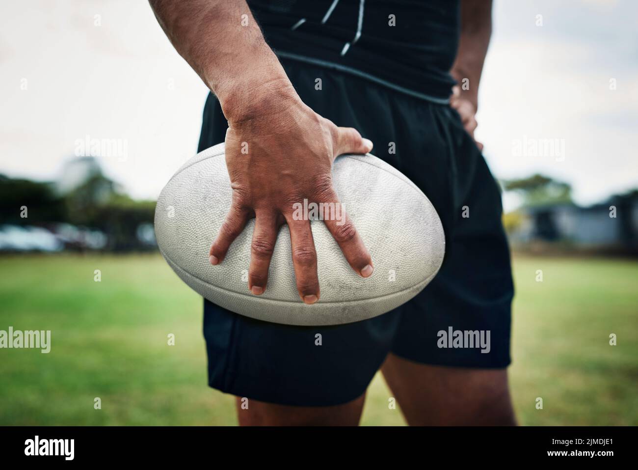 Jouer avec ce ballon est sa chose préférée. Un joueur de rugby méconnaissable tenant un ballon de rugby sur le terrain pendant la journée. Banque D'Images