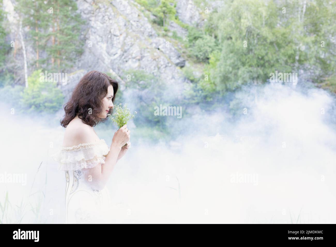 Belle fille avec cheveux foncés dans le brouillard avec des fleurs. Banque D'Images