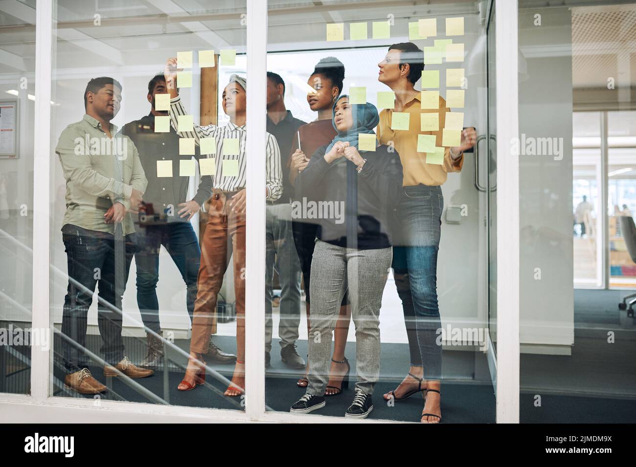 Planifiez bien pour réussir. Un groupe de professionnels remue-méninges avec des notes sur un mur de verre dans un bureau. Banque D'Images