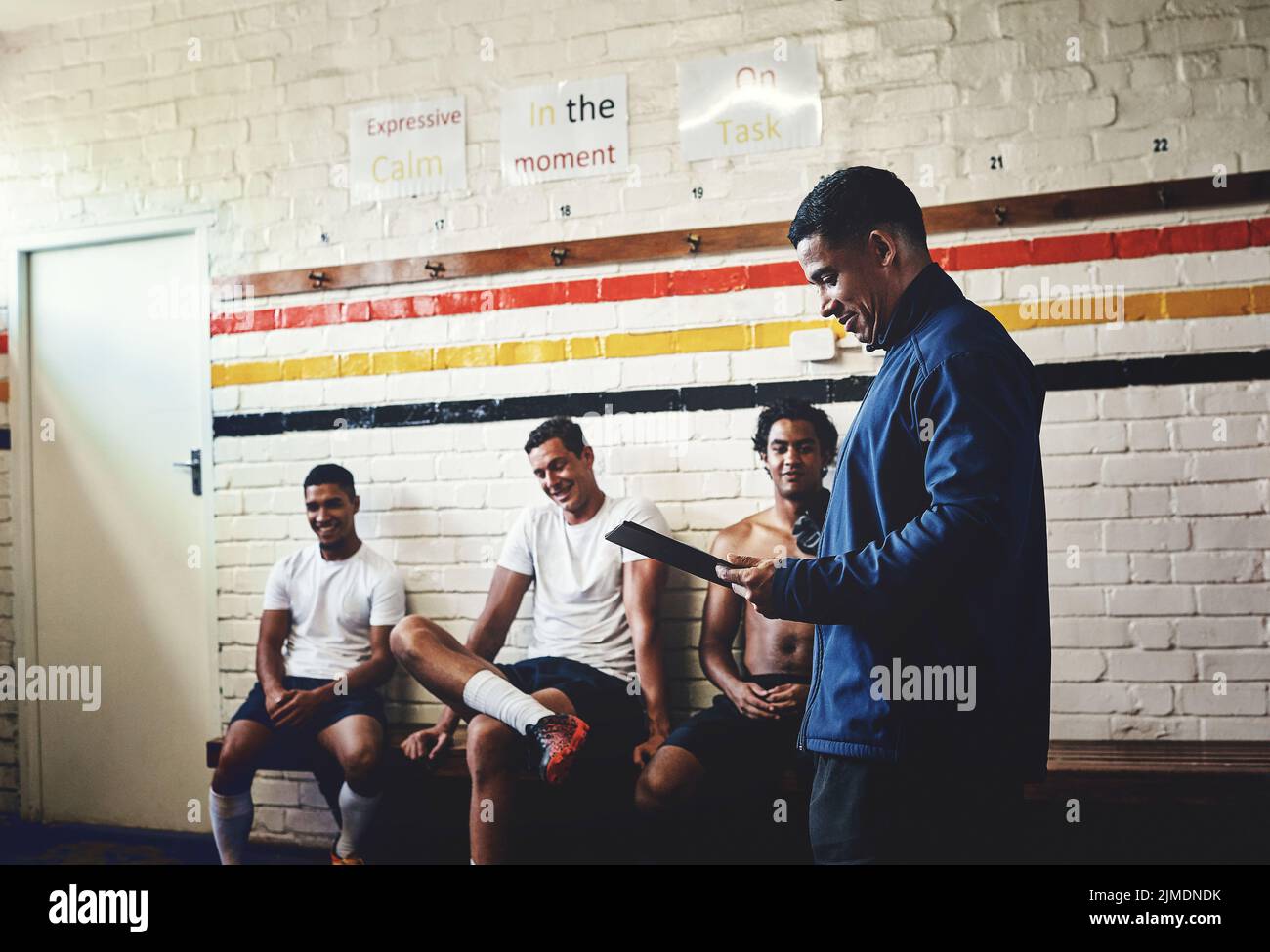 Eh bien les gars, disons que j'ai de bonnes nouvelles pour vous. Un entraîneur de rugby s'adressant à ses joueurs de l'équipe dans un vestiaire pendant la journée. Banque D'Images