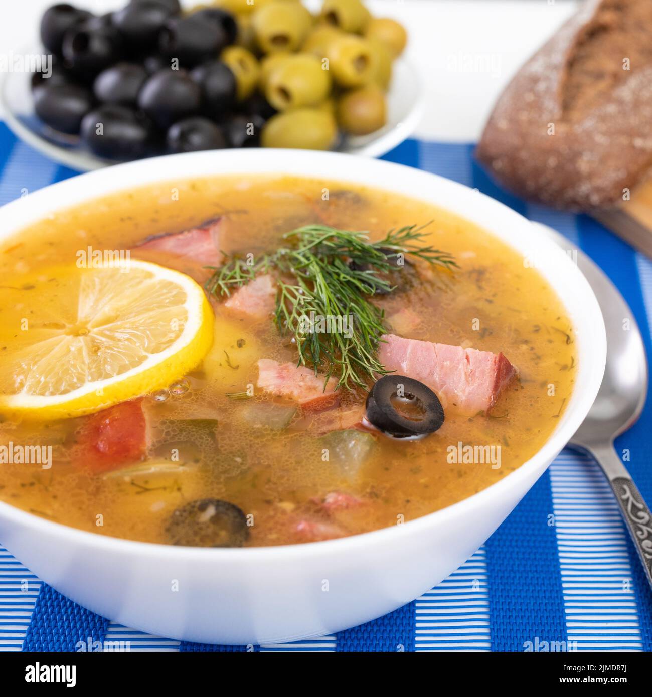 Soupe russe traditionnelle Solyanka cuite avec de la viande, des saucisses, des concombres salés sur un bol de wite. Pain noir, citron, oled et toma Banque D'Images