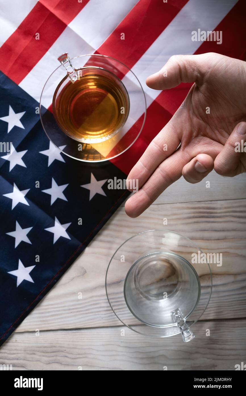 Table séparée par un drapeau américain avec une tasse pleine et une tasse vide sur la table et la main de l'homme en position V. Banque D'Images