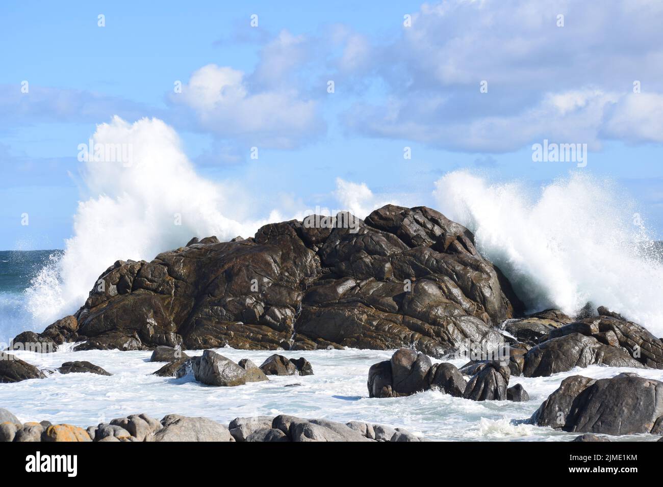 Des nuages touchant la mer, mélangeant le blanc, le bleu et le gris. Les roches et le bassin marécageux en premier plan font écho à la grande roche et à la mousse du point focal. Banque D'Images