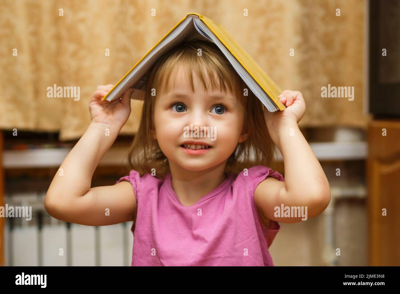 Petite sourit une jolie fille avec un livre ouvert sur sa tête Banque D'Images