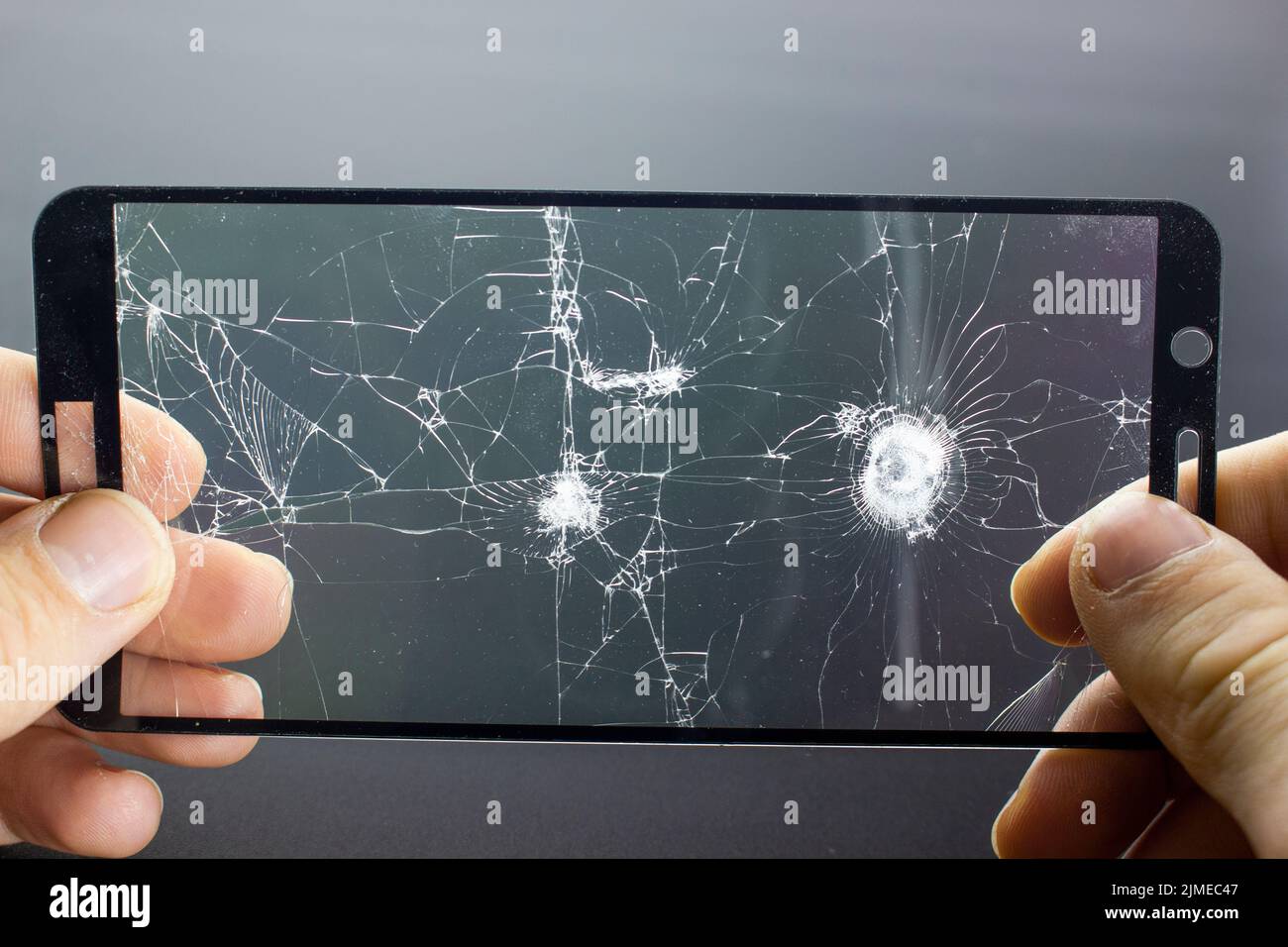 Verre de protection cassé du smartphone avec des fissures dans les mains sur fond noir. Banque D'Images