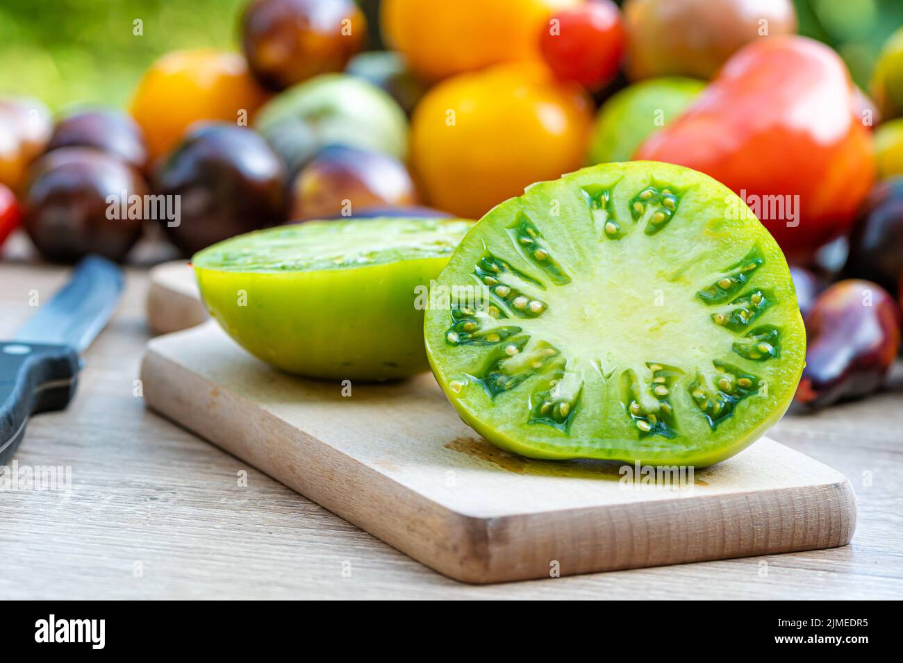 table avec une planche à découper avec des tomates en tranches et des tomates de différentes couleurs en arrière-plan Banque D'Images
