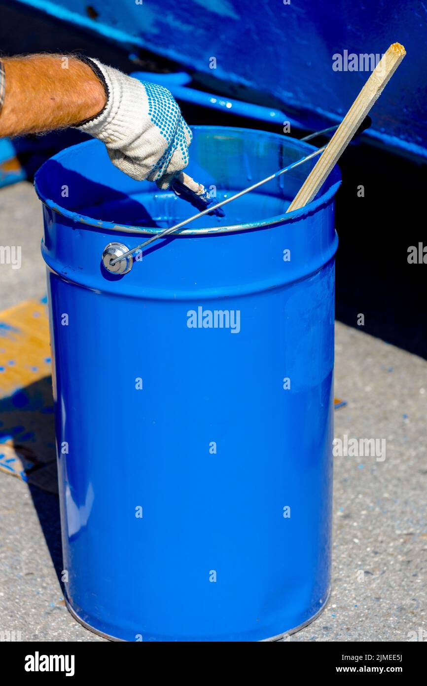 Seau en métal avec peinture bleue. Une main dans un gant de protection peut contenir une brosse à peinture. Banque D'Images