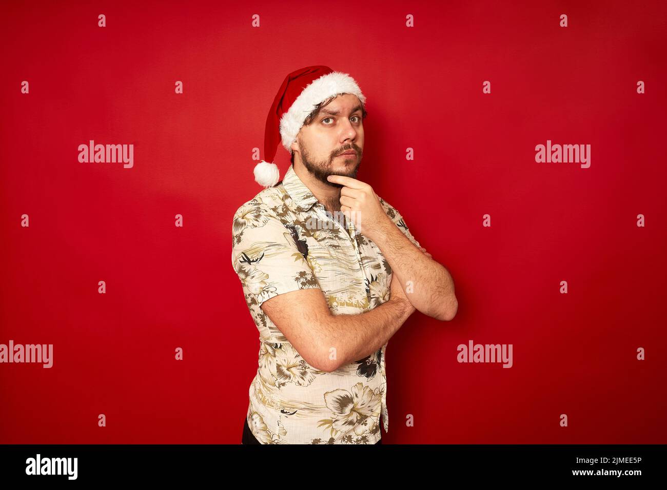 Un homme sérieux et attentionné touriste en chapeau de Noël, mettez la main au menton en posant de réflexion Banque D'Images