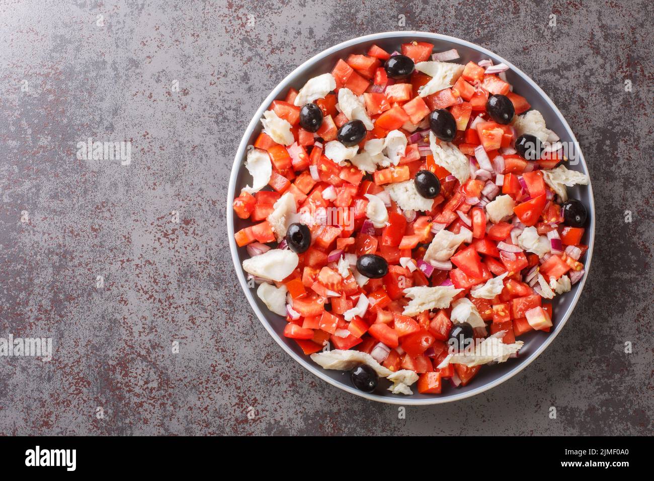 Salade espagnole de cabillaud salé, tomates fraîches, oignons et olives noires dans une assiette sur la table. Vue horizontale du dessus Banque D'Images