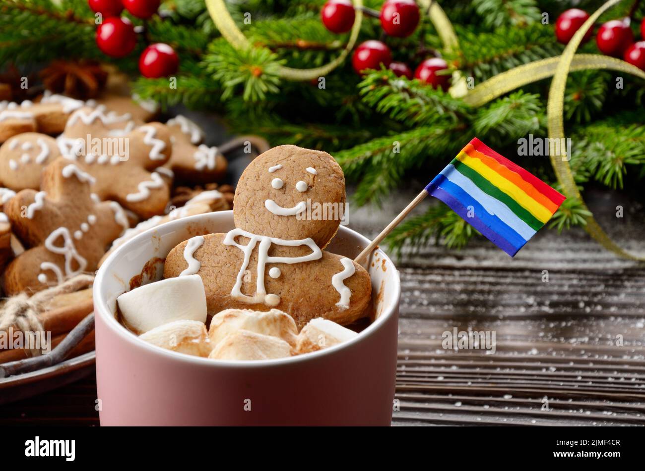 Tasse rose avec guimauves au chocolat chaud et homme de pain d'épice avec drapeau arc-en-ciel sur fond de branche d'épinette et plateau avec cuisinière Banque D'Images