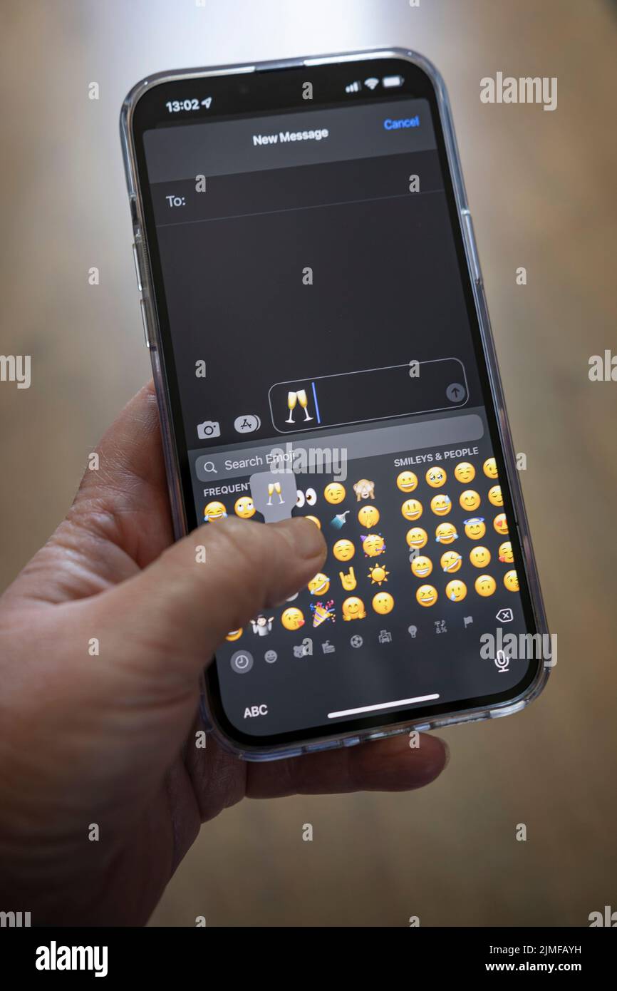 IPhone 13 pro max étant tenu avec une main caucasienne textant un clinking champaign verre emoji Banque D'Images