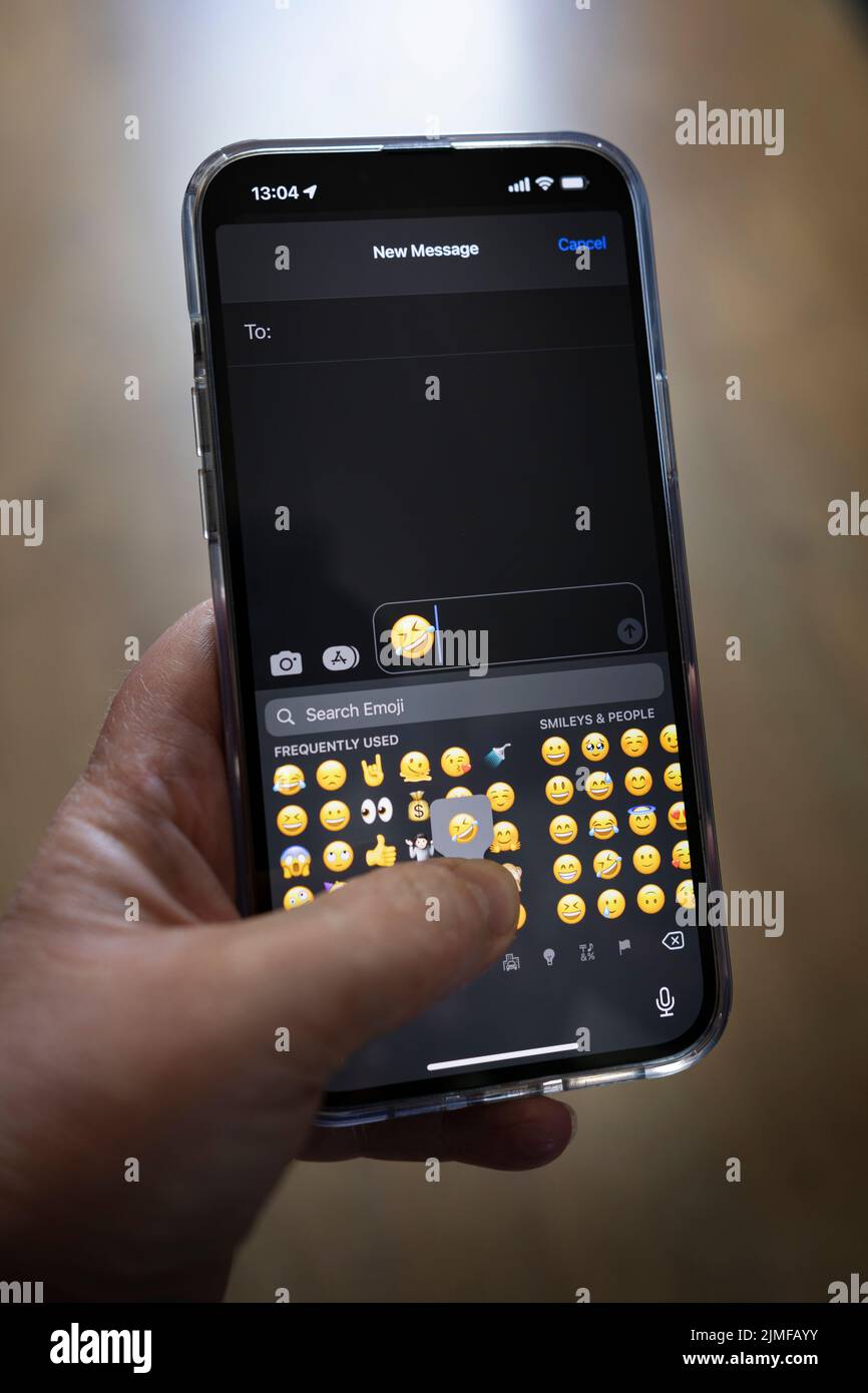 IPhone 13 pro max étant tenu avec une main caucasienne textant une pleurs avec le rire emoji Banque D'Images