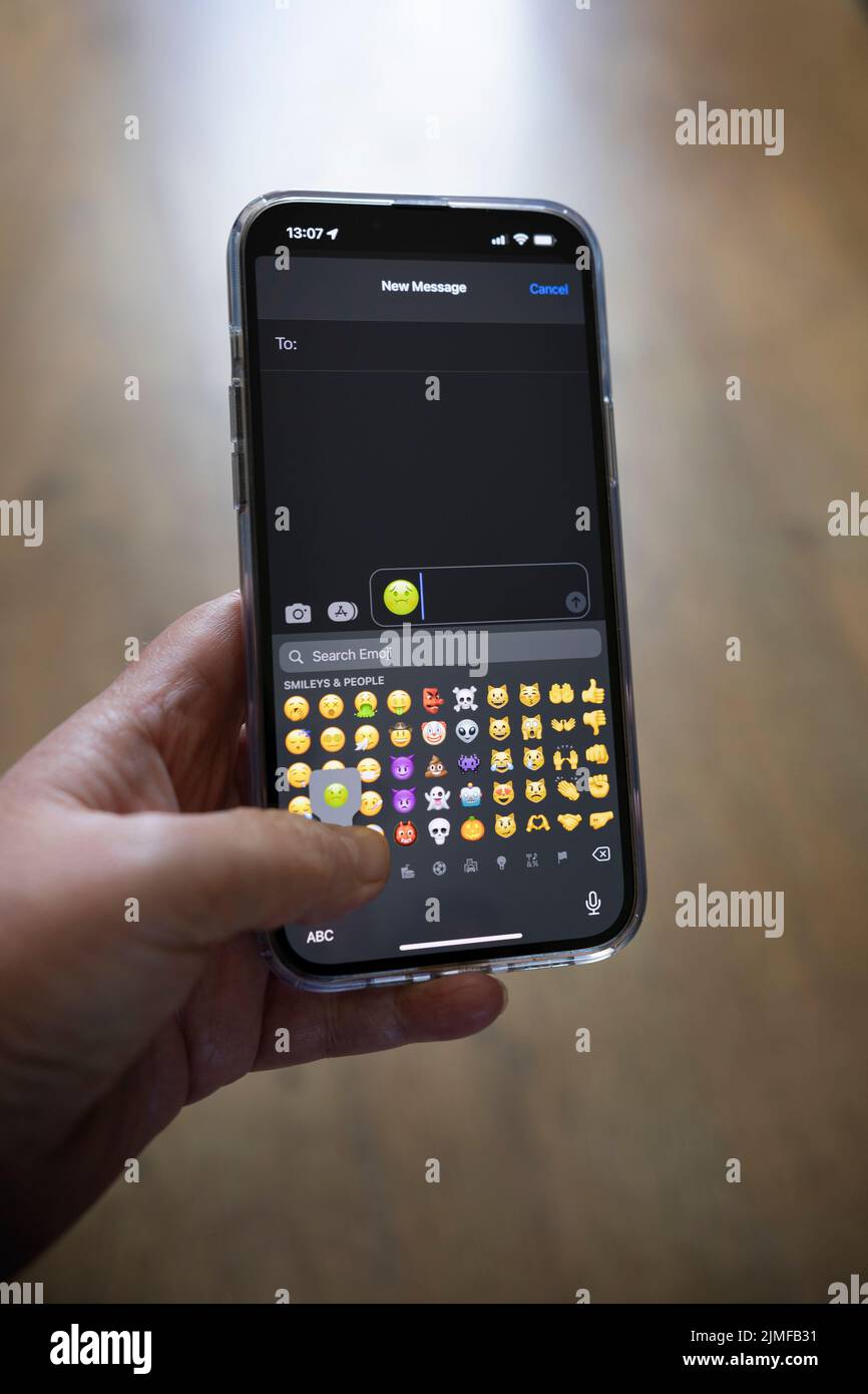 IPhone 13 pro max étant tenu avec une main caucasienne textant un sentiment vert malade emoji Banque D'Images