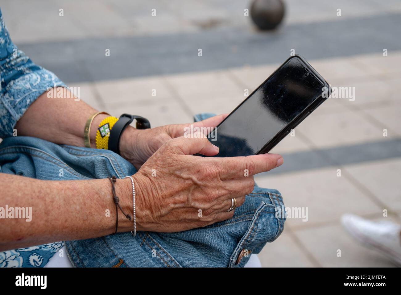 Gros plan d'une femme plus âgée avec des bracelets portant un smartphone noir Banque D'Images