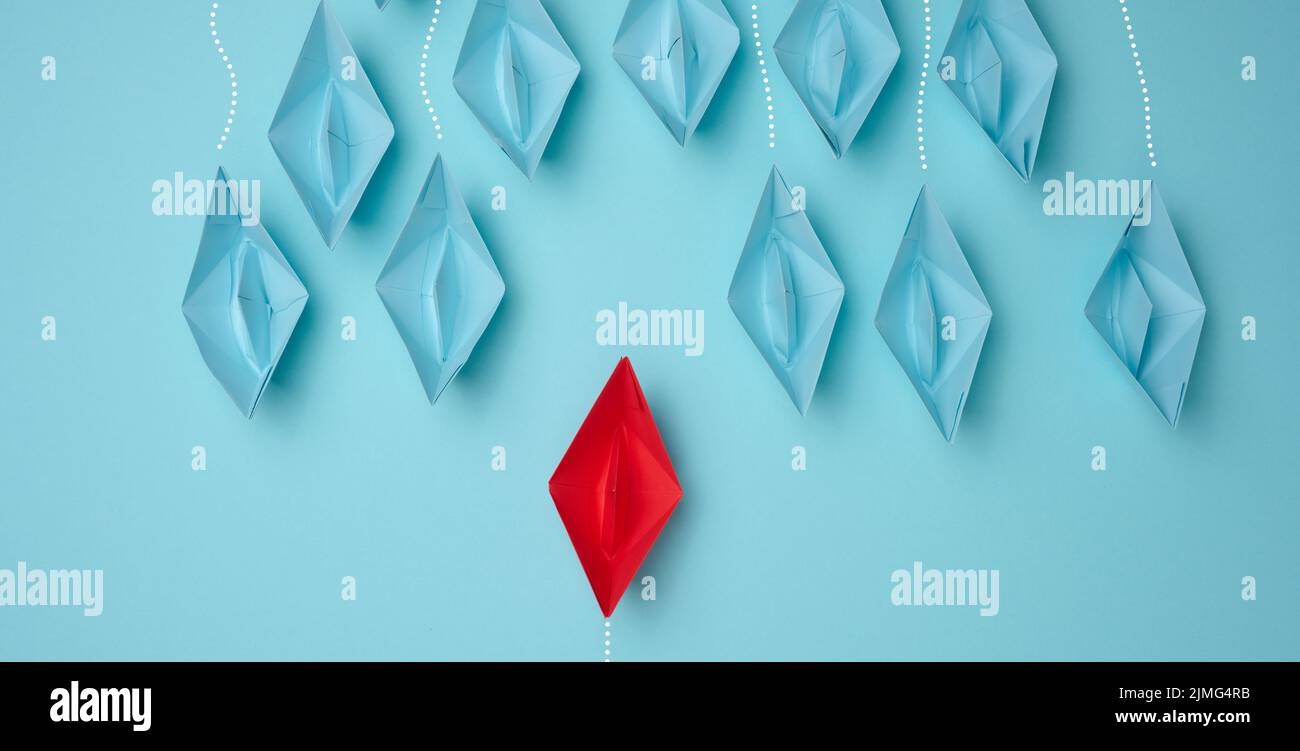 Un groupe de bateaux en papier bleu se dirigeant dans une direction et un rouge se dirigeant dans la direction opposée. Le concept de l'individua Banque D'Images